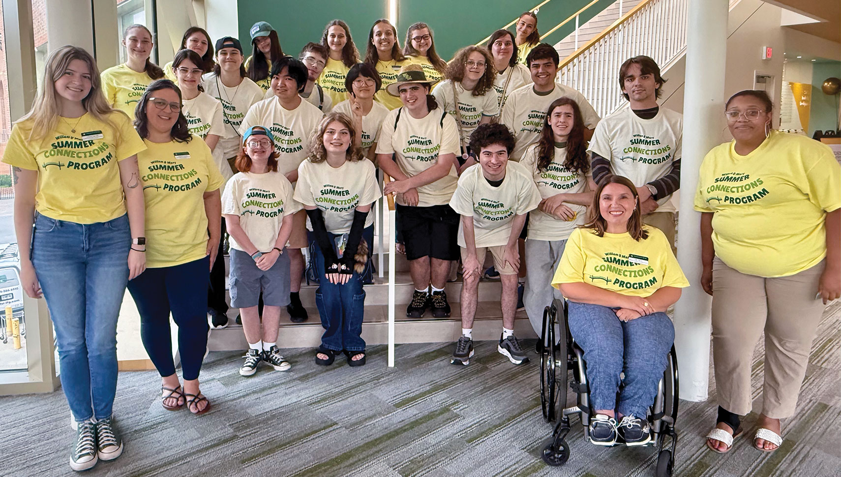 New first-year and transfer students in William & Mary's Summer Connections pre-orientation program posing with student mentors and staff from Student Accessibility Services on a campus staircase, wearing matching Summer Connections program shirts