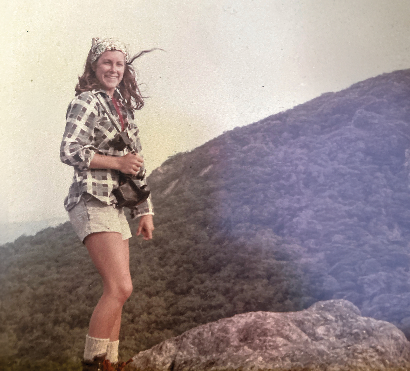 aged photo of woman standing on rock with mountain in background
