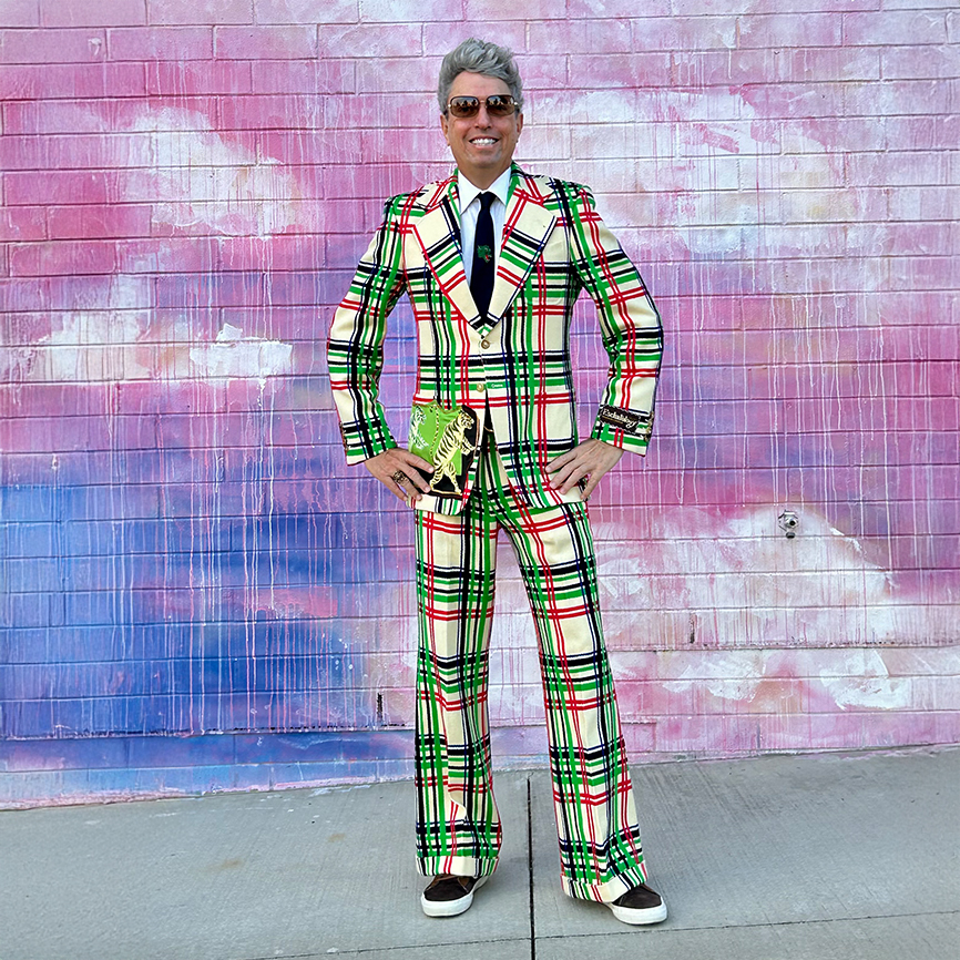man standing in front of pastel mural in a brightly colored plaid suit