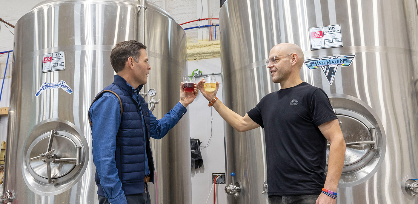Will Payne and his twin brother, Jud Payne ’01 (right), toast in front of cider vats named after legendary rock bands