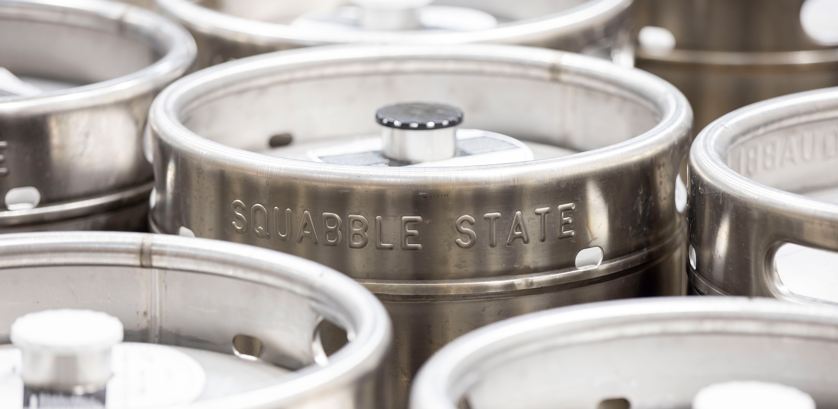 A closeup of stainless steel kegs with Squabble State on the side