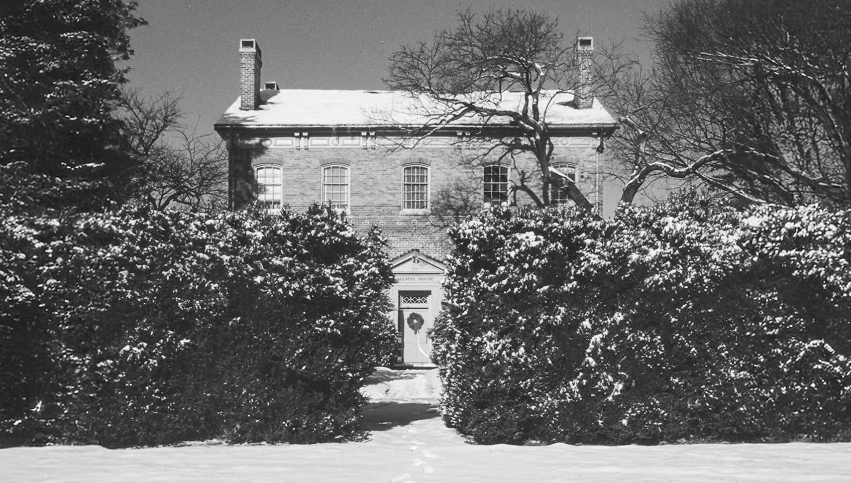 black and white photo of alumni house covered in snow with footprints leading from the doorway