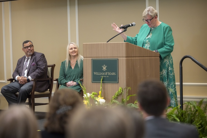 Photo of a woman giving a speech while others look on.